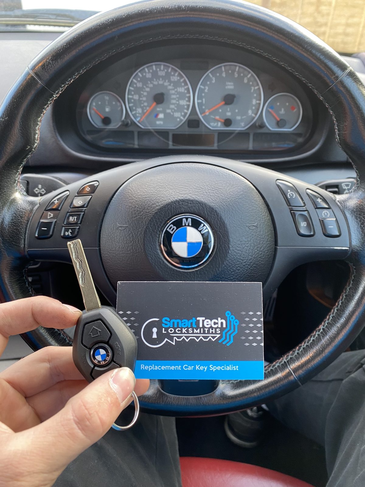 BMW 3 Series spare key in Hampshire by SmartTech Auto Locksmiths, key and business card held in front of the vehicle