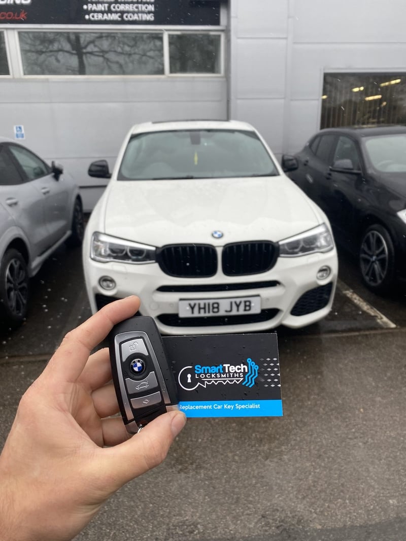 BMW X4 smart key programmed in Hampshire by SmartTech Auto Locksmiths, key and business card held in front of the vehicle