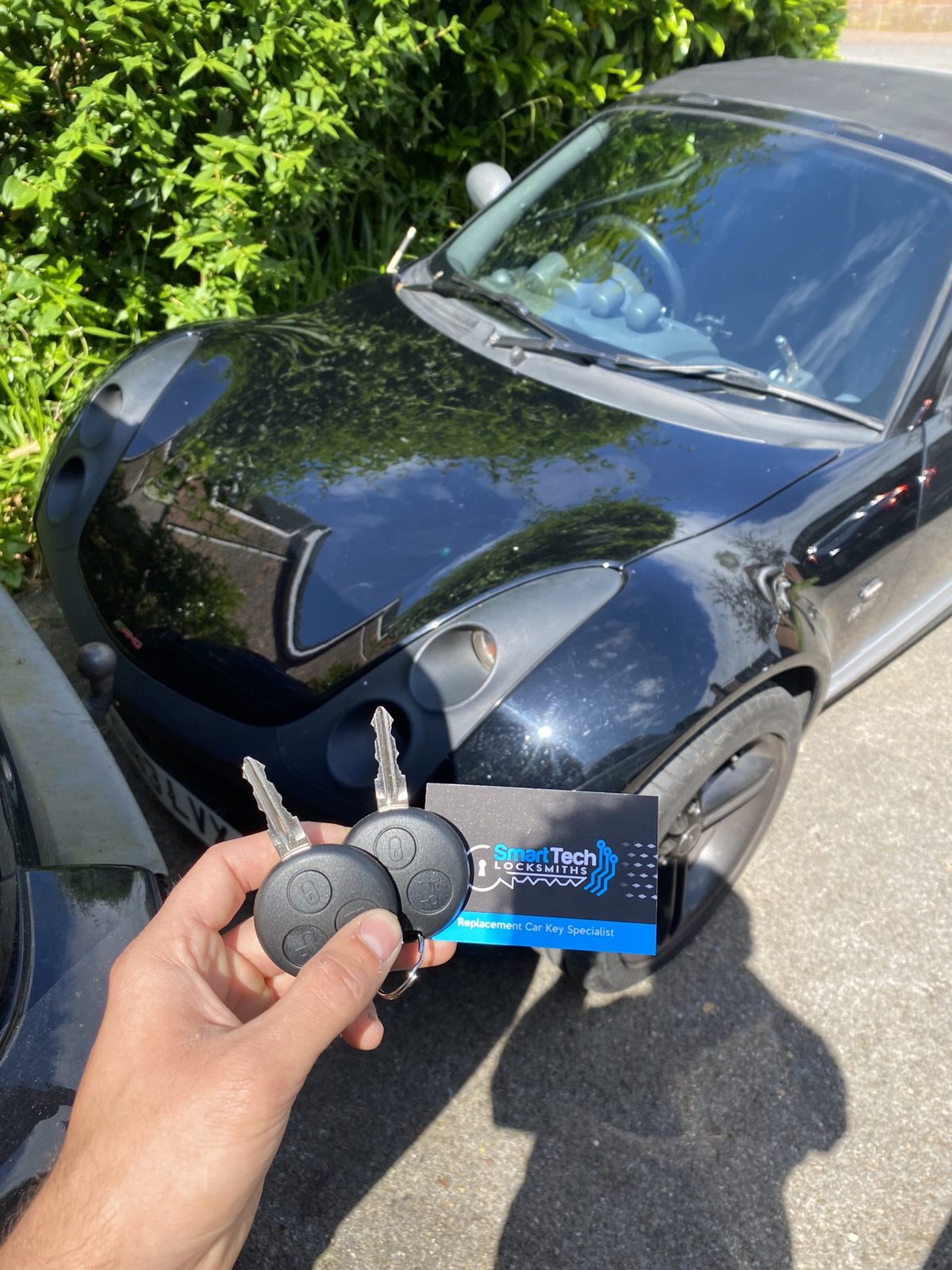 Smart ForTwo two keys cut and coded in Hampshire by SmartTech Auto Locksmiths, key and business card held in front of the vehicle