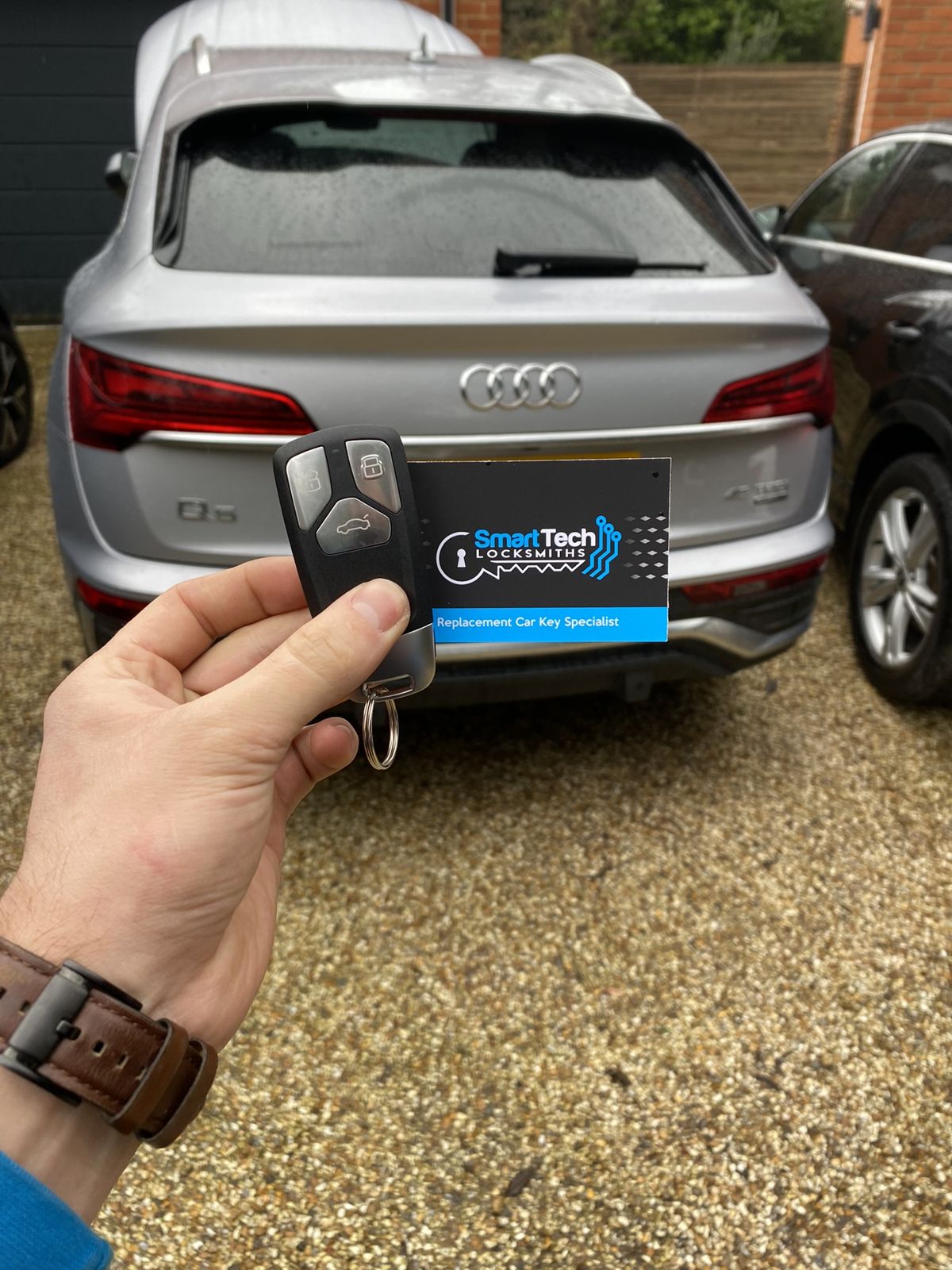 Audi Q5 smart key programmed in Salisbury by SmartTech Auto Locksmiths, key and business card held in front of the vehicle