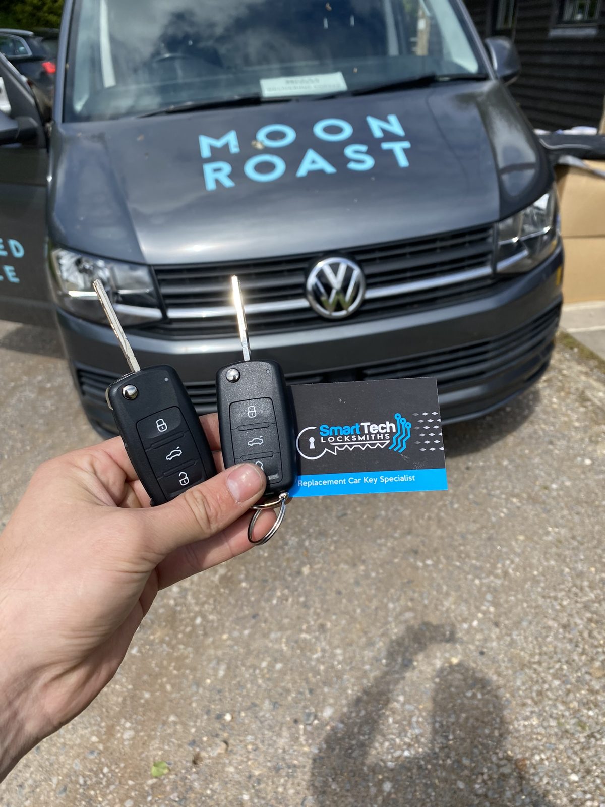 Volkswagen Transporter T6 two flip keys cut and coded in Hampshire by SmartTech Auto Locksmiths, key and business card held in front of the vehicle