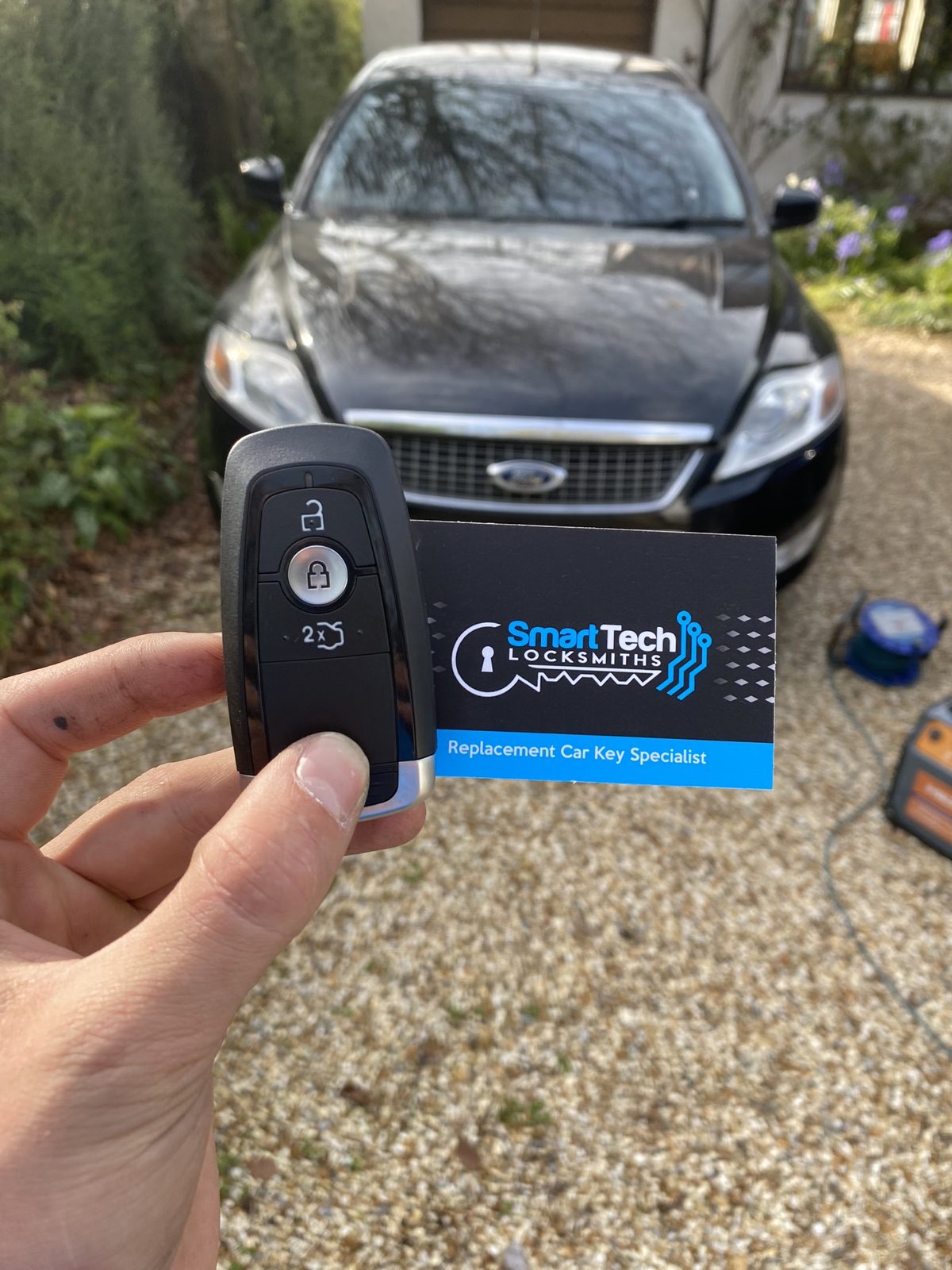 Ford Mondeo smart key programmed in Hampshire by SmartTech Auto Locksmiths, key and business card held in front of the vehicle