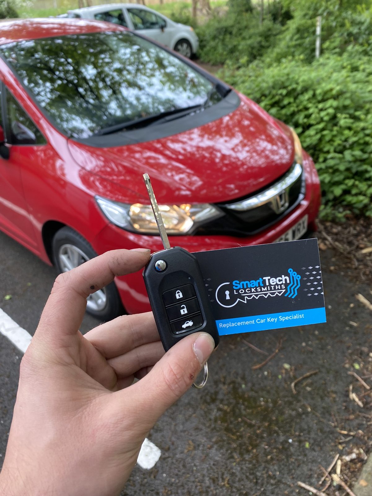 Honda Jazz flip key cut and coded in Hampshire by SmartTech Auto Locksmiths, key and business card held in front of the vehicle