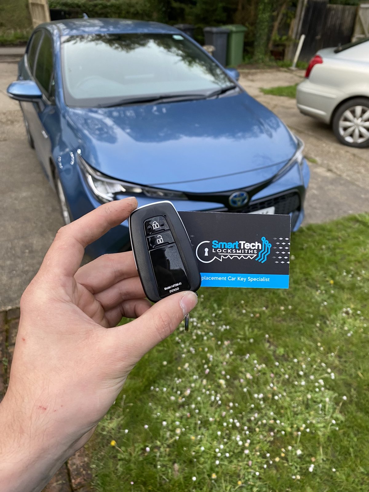Toyota Prius smart key programmed in Hampshire by SmartTech Auto Locksmiths, key and business card held in front of the vehicle