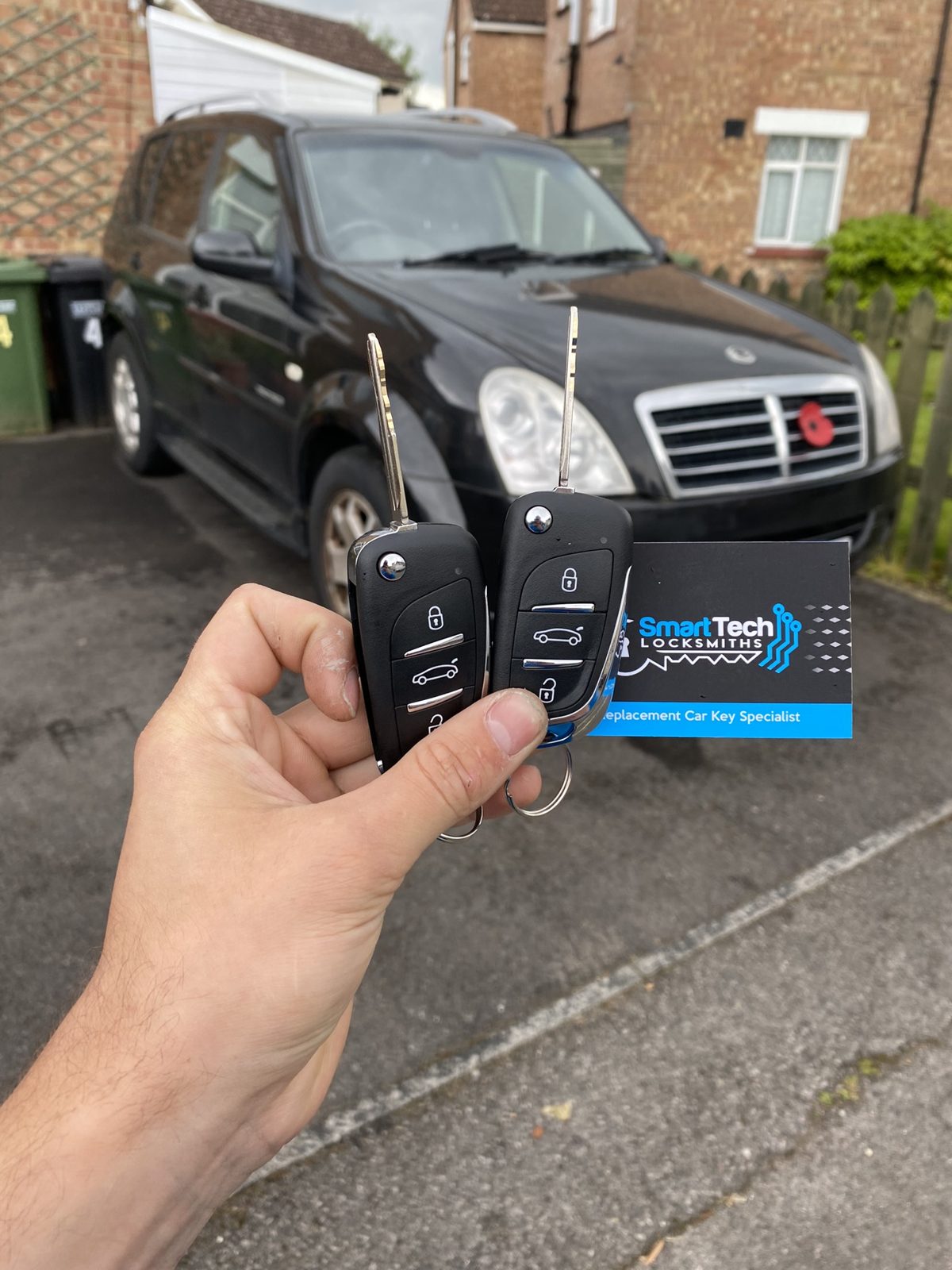 SsangYong Rexton two flip keys cut and coded in Hampshire by SmartTech Auto Locksmiths, key and business card held in front of the vehicle