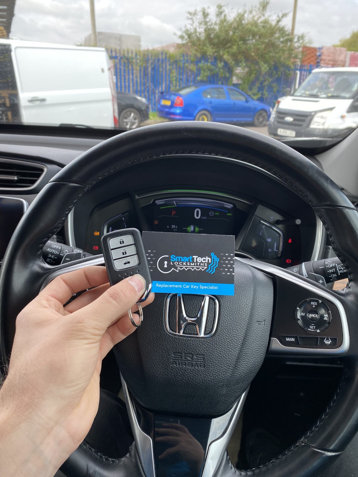 Honda smart key programmed in Hampshire by SmartTech Auto Locksmiths, key and business card held in front of the vehicle