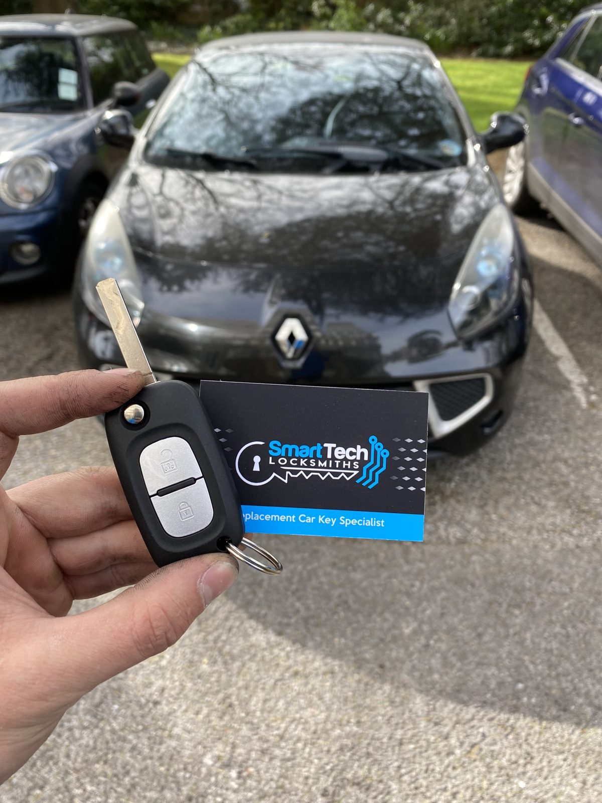 Renault Clio flip key cut and coded in Hampshire by SmartTech Auto Locksmiths, key and business card held in front of the vehicle
