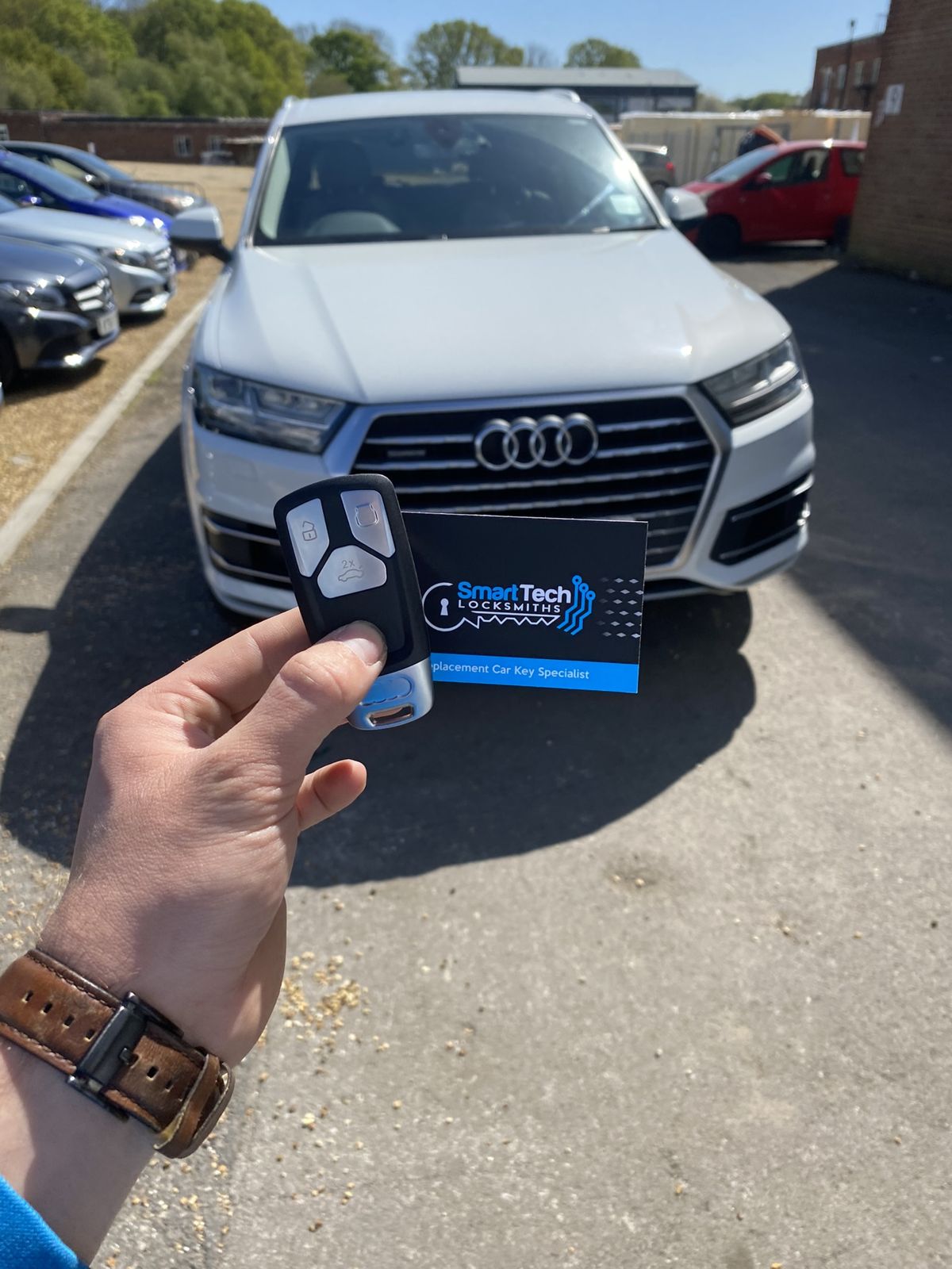 Audi Q7 spare remote key in Salisbury by SmartTech Auto Locksmiths, key and business card held in front of the vehicle