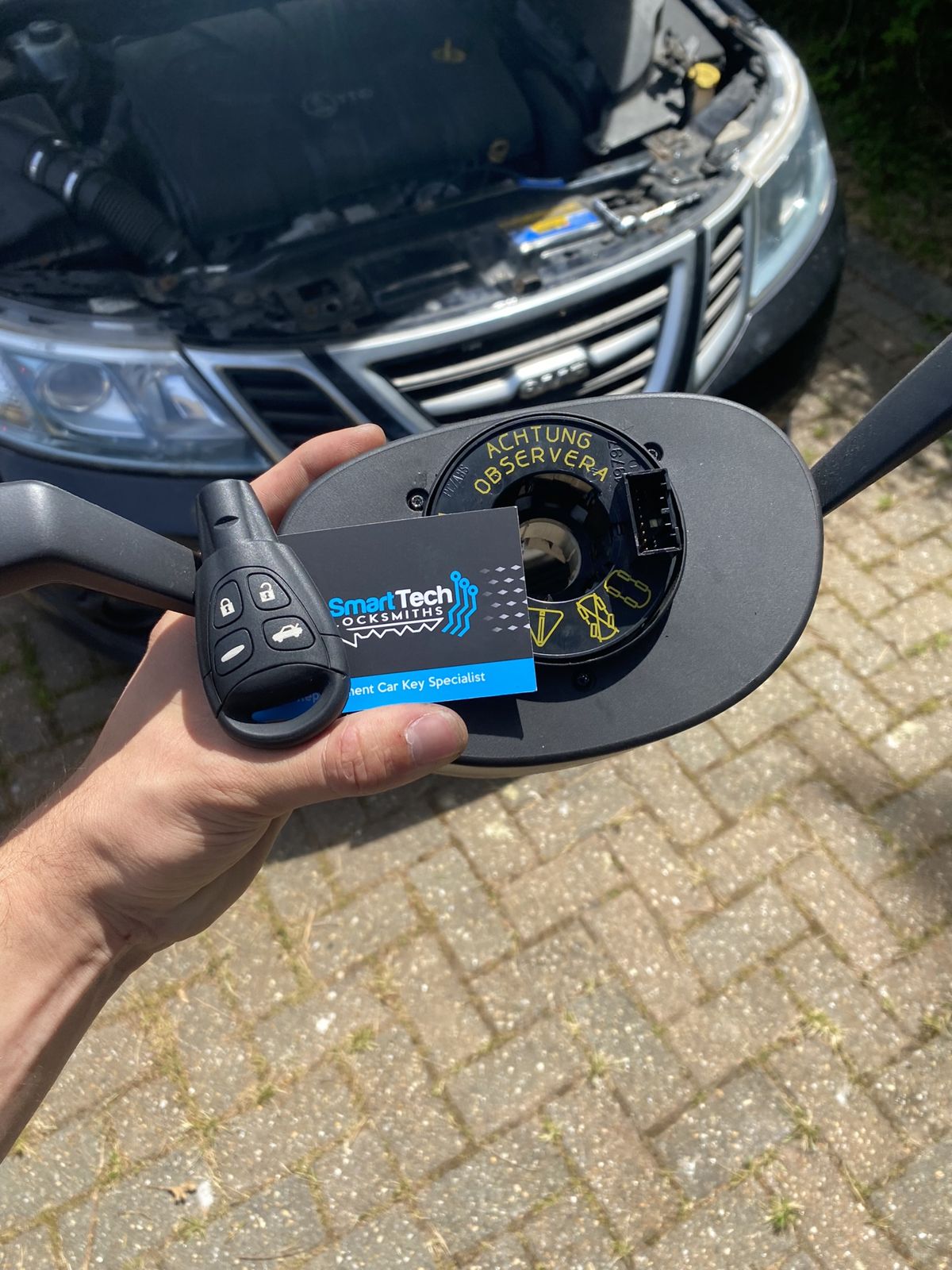Saab 9-3 steering lock and key repair in Hythe & Dibden Purlieu by SmartTech Auto Locksmiths, key and business card held in front of the vehicle