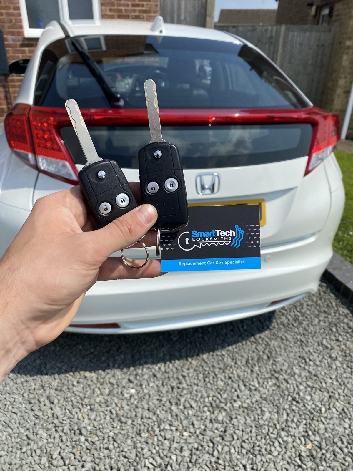 Honda Civic two flip keys cut and coded in Hampshire by SmartTech Auto Locksmiths, key and business card held in front of the vehicle