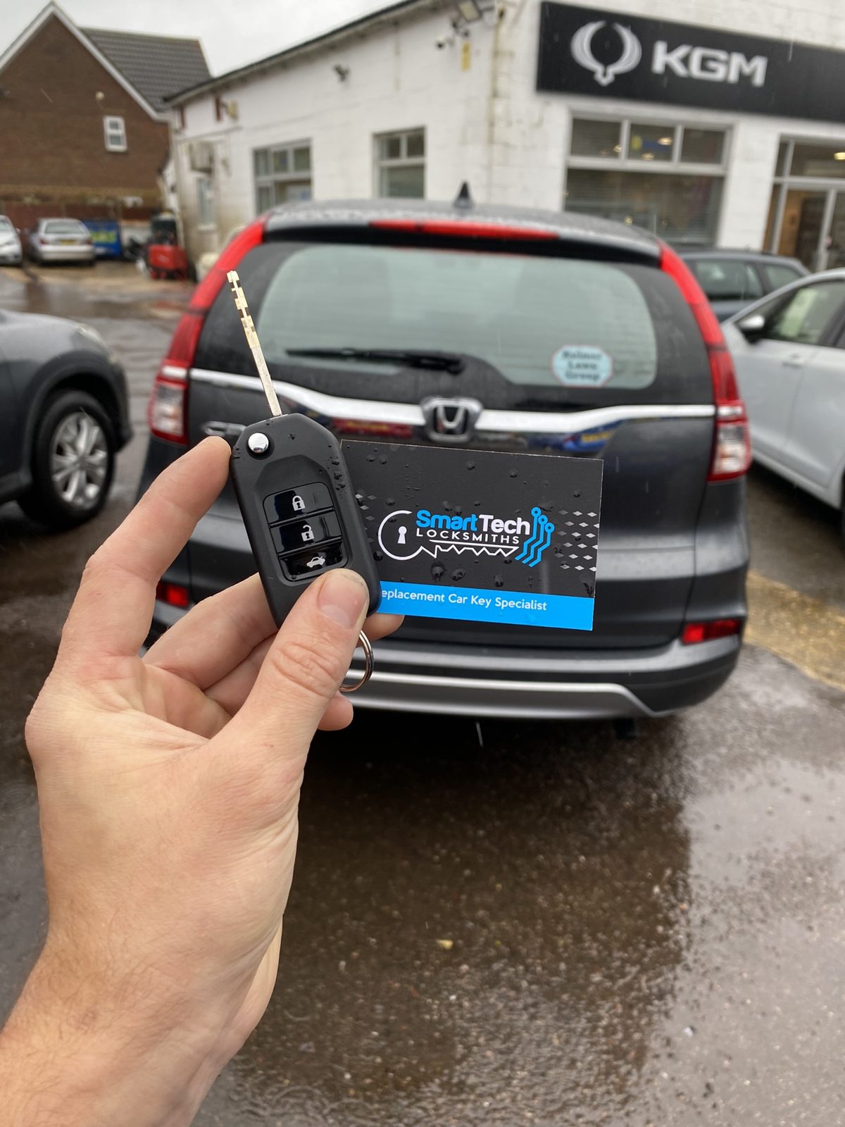 Honda CR-V flip key cut and coded in Hampshire by SmartTech Auto Locksmiths, key and business card held in front of the vehicle