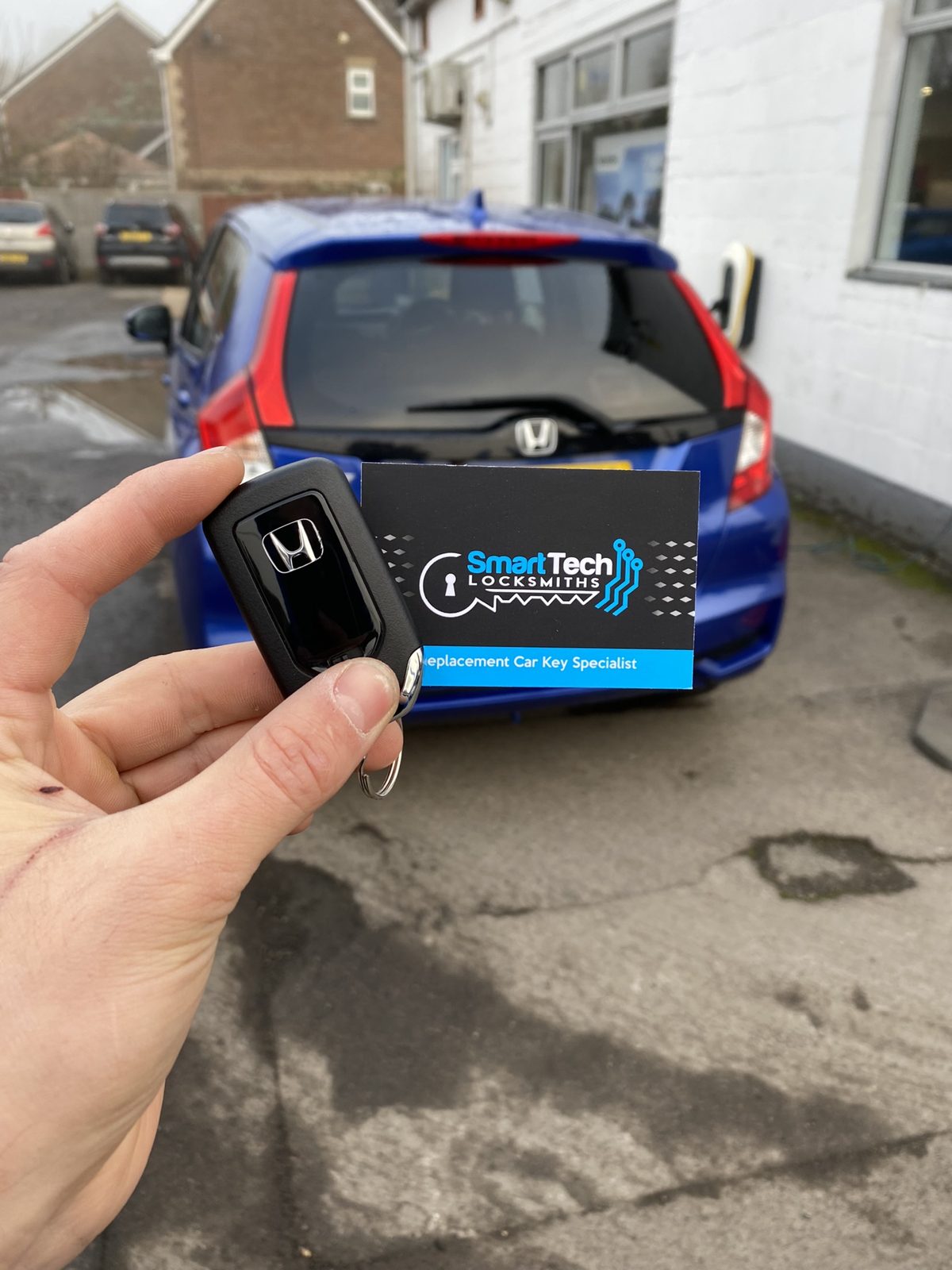 Honda Jazz smart key programmed in Eastleigh by SmartTech Auto Locksmiths, key and business card held in front of the vehicle