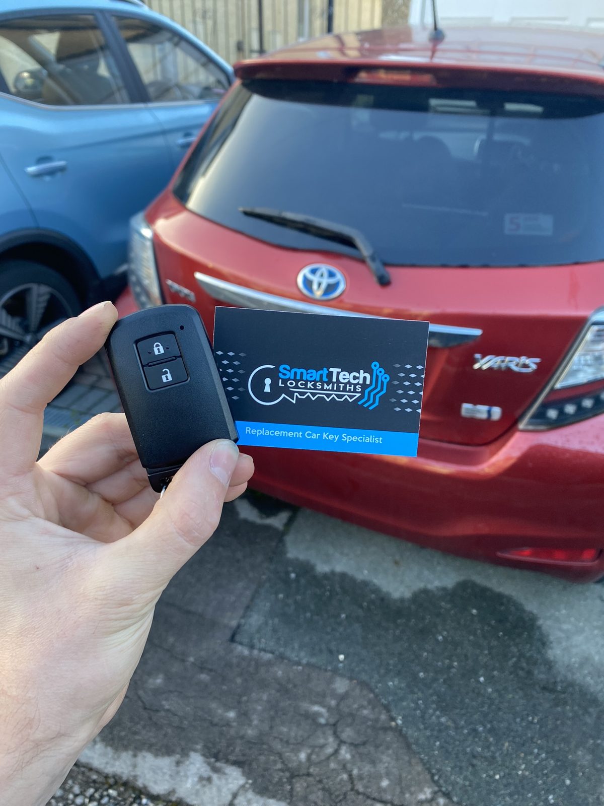 Toyota Yaris smart key programmed in Hampshire by SmartTech Auto Locksmiths, key and business card held in front of the vehicle
