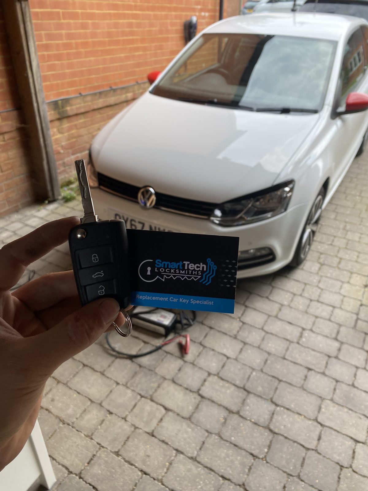 Volkswagen Polo flip key cut and coded in Hampshire by SmartTech Auto Locksmiths, key and business card held in front of the vehicle