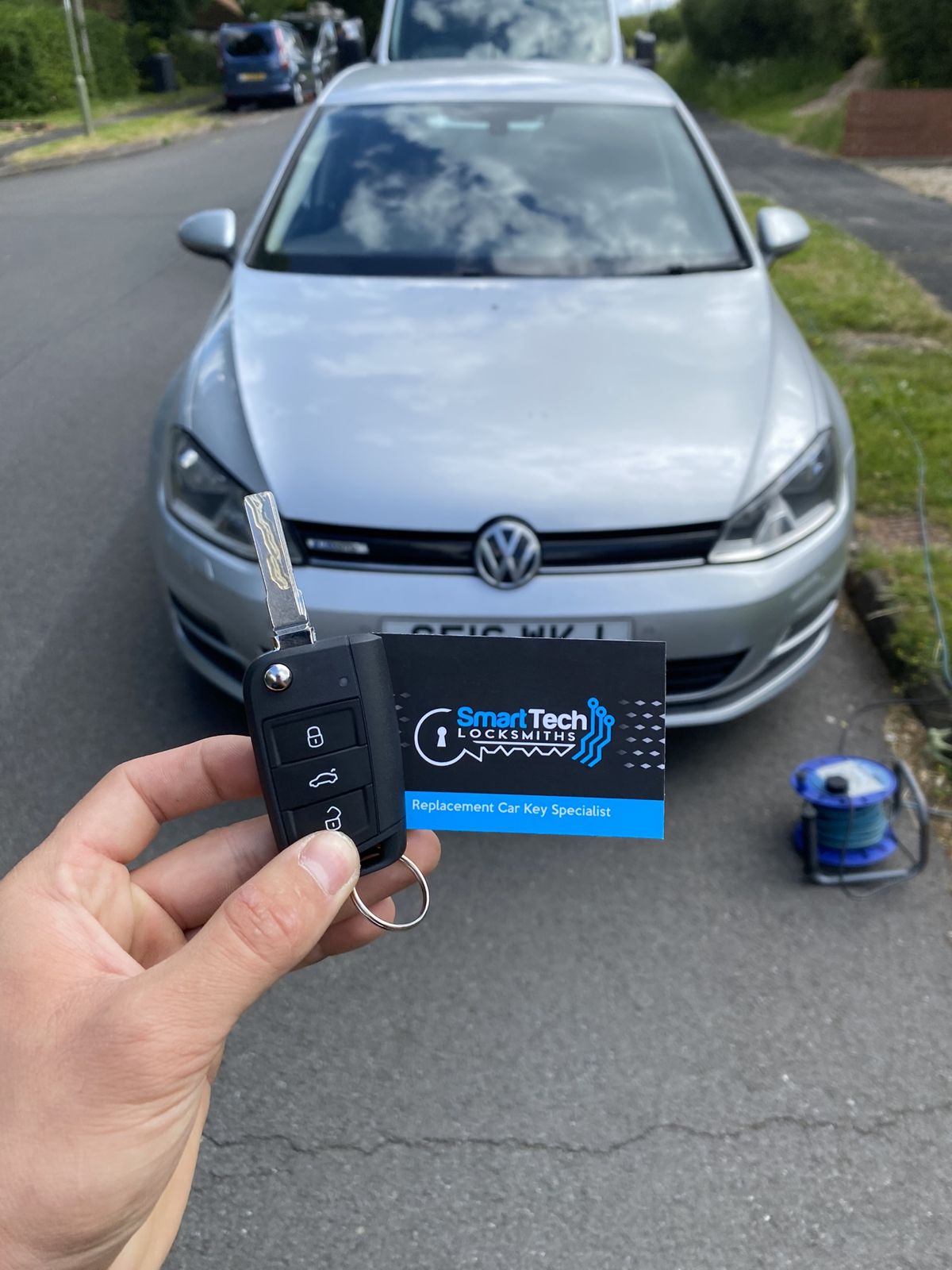 Volkswagen Golf spare flip key in Salisbury by SmartTech Auto Locksmiths, key and business card held in front of the vehicle