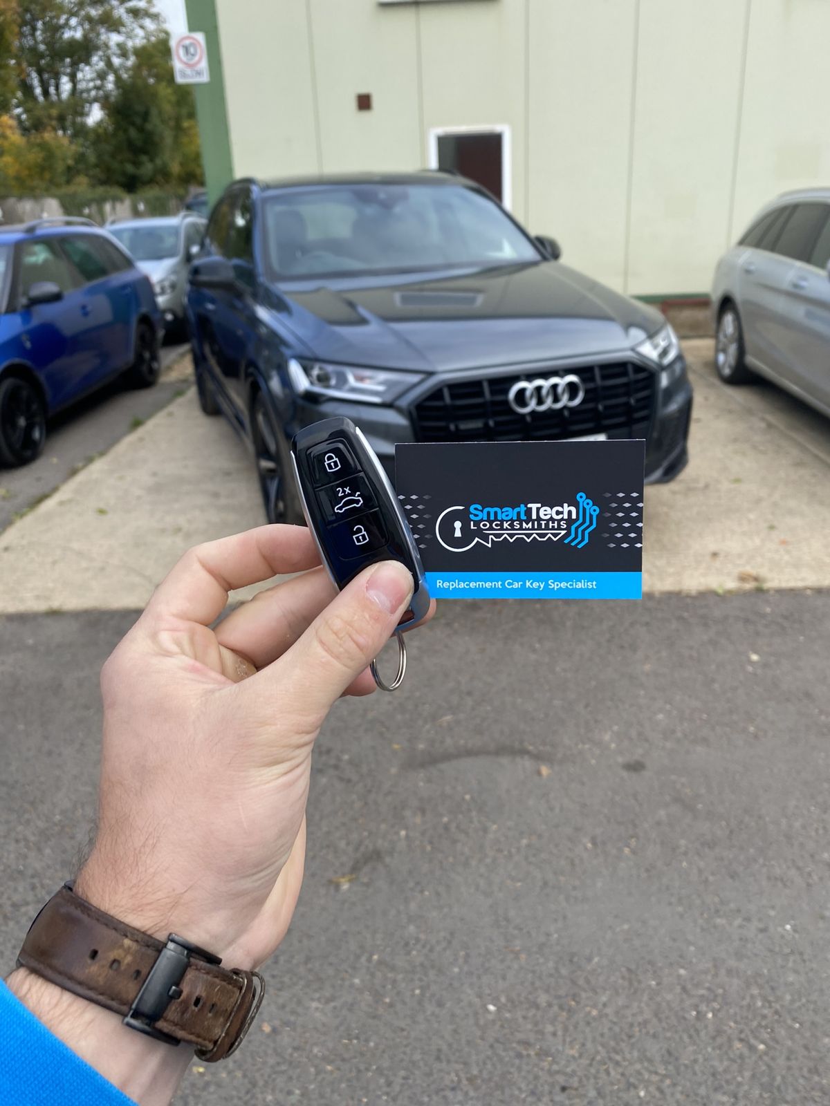 Audi Q7 smart key programmed in Eastleigh by SmartTech Auto Locksmiths, key and business card held in front of the vehicle