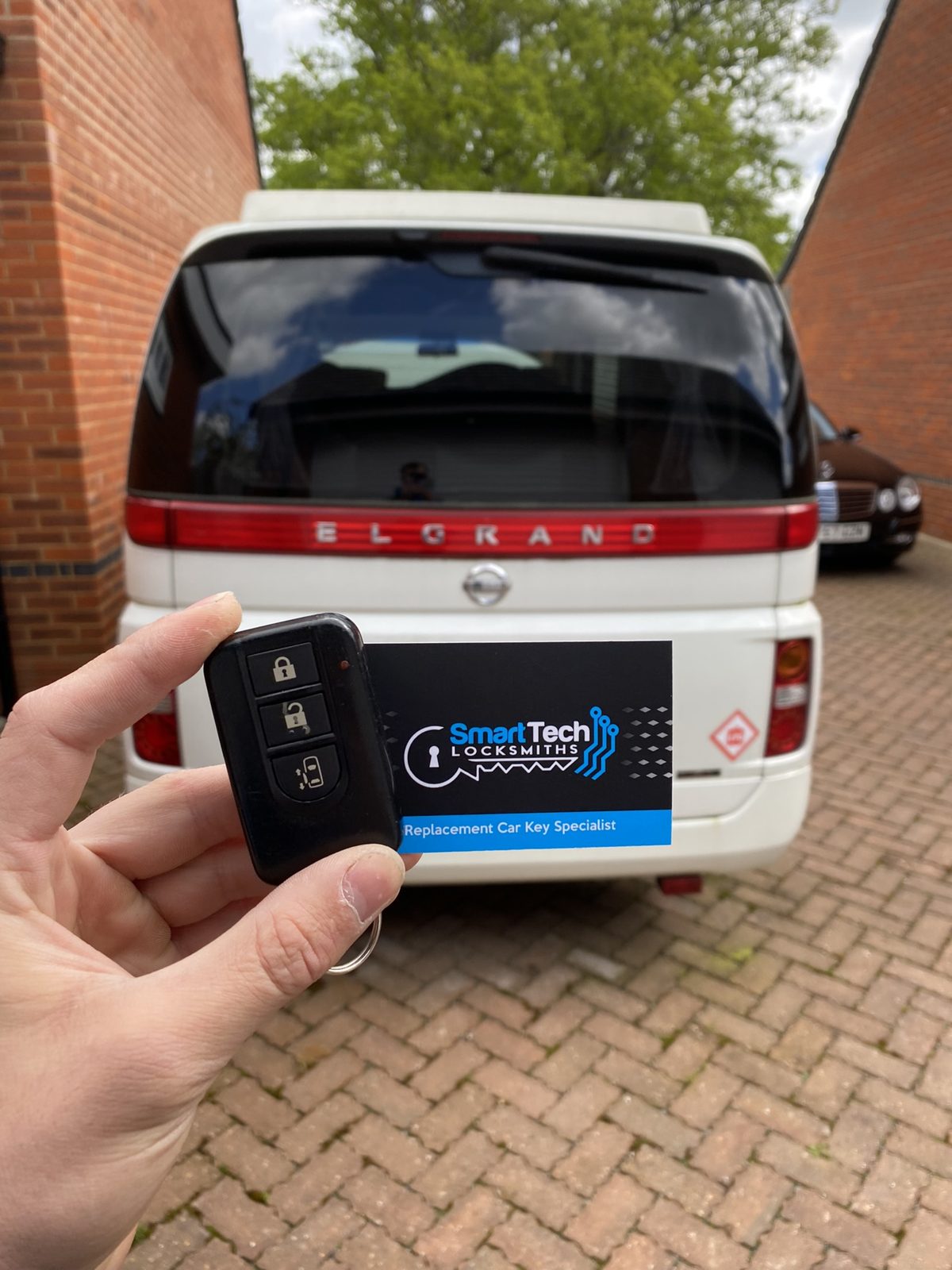Nissan Elgrand replacement smart key in Hampshire by SmartTech Auto Locksmiths, key and business card held in front of the vehicle