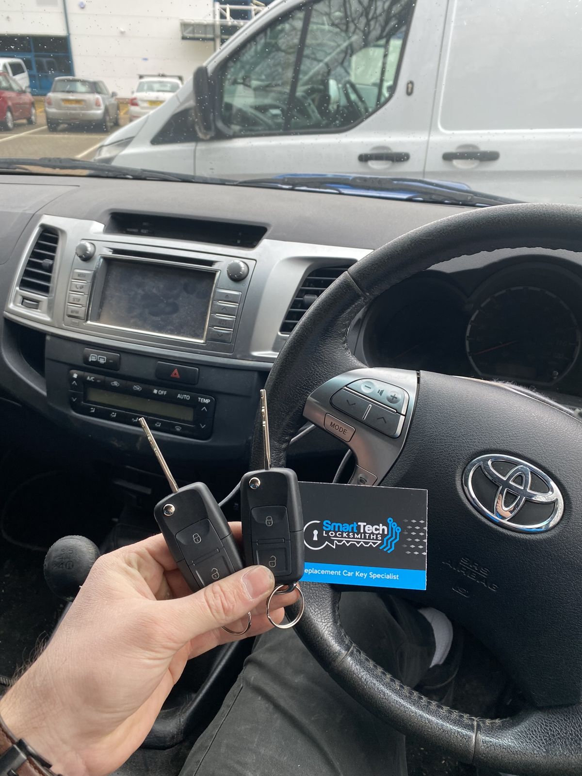 Toyota Hilux two keys cut and coded in Southampton by SmartTech Auto Locksmiths, key and business card held in front of the vehicle