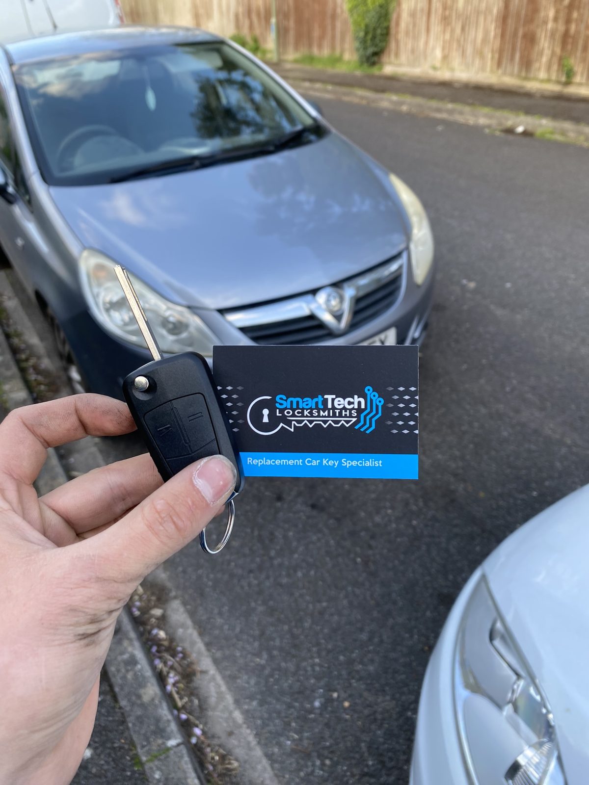 Vauxhall Corsa flip key cut and coded in Hampshire by SmartTech Auto Locksmiths, key and business card held in front of the vehicle